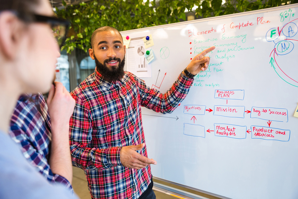 Happy afro american presenting business plan on whiteboard to his colleagues in office